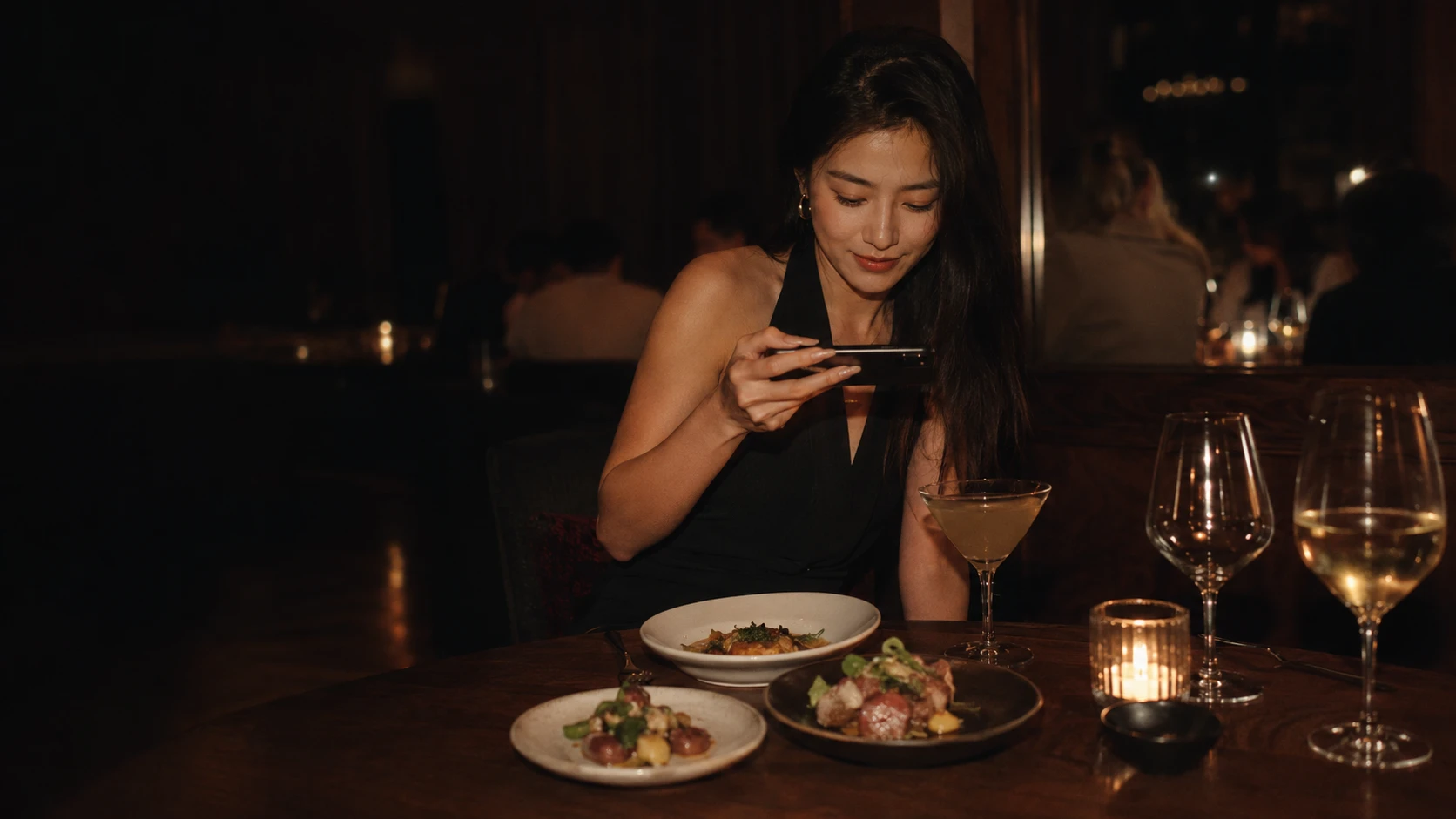 A diner photographing her plates on a phone by candlelight in a dark restaurant